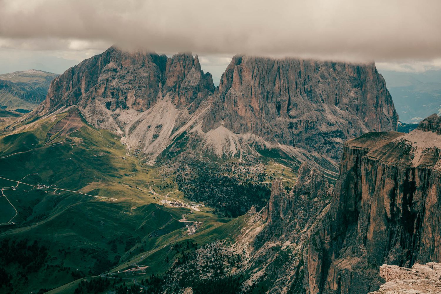 Dramatic Dolomite mountains with jagged rocky peaks, winding road, and moody overcast sky in the Italian Alps.