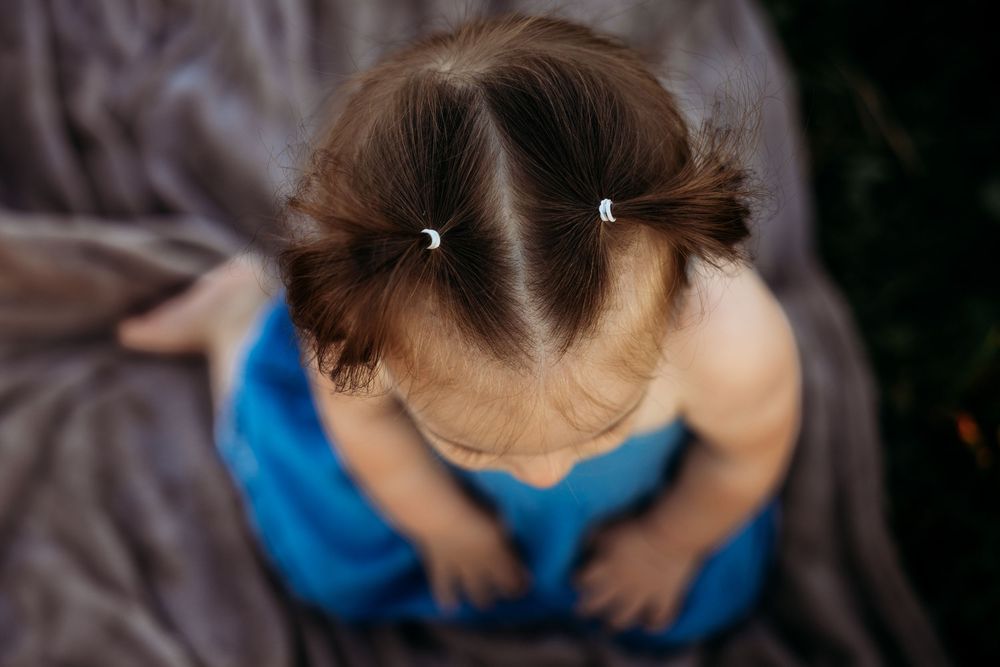 Aerial view of a toddler girl with brown hair in two small pigtails wearing a blue dress.