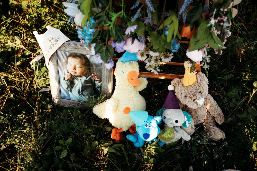 Memorial with baby photo, stuffed animals, and flowers arranged on grass as a touching tribute.