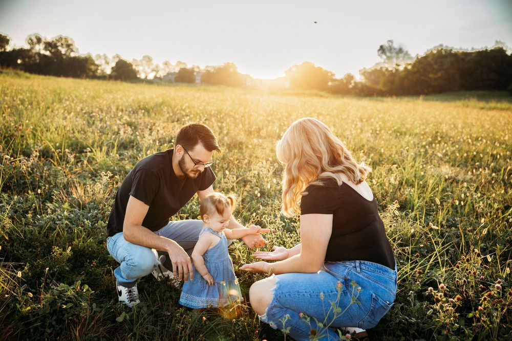 Family with young child enjoying golden hour sunset in a green meadow field together.