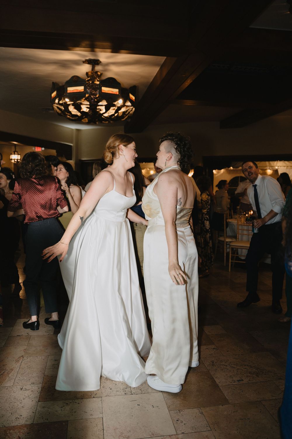 Two brides in white gowns share a joyful dance together at their wedding reception.