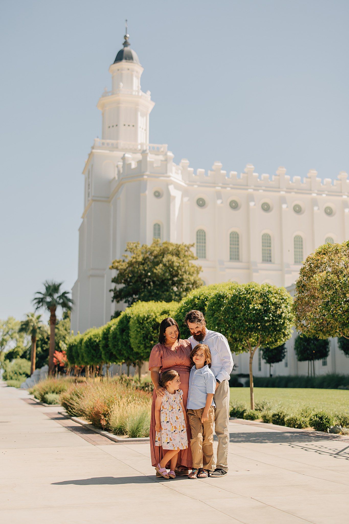 Family of four posing together on a sunny day outside the white St. George Utah LDS Temple.