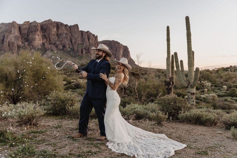 Couple celebrating wedding in Arizona desert with saguaro cacti and mountain backdrop at dusk.