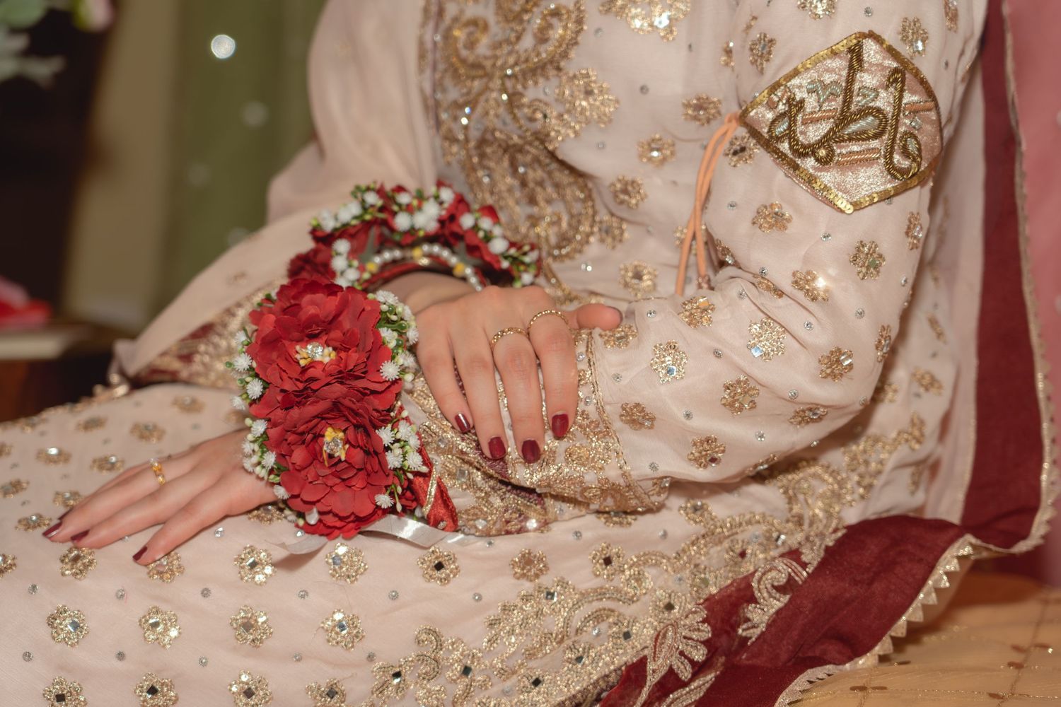 Bride in embroidered white and red South Asian bridal outfit holding a floral bouquet with mehndi-adorned hands.
