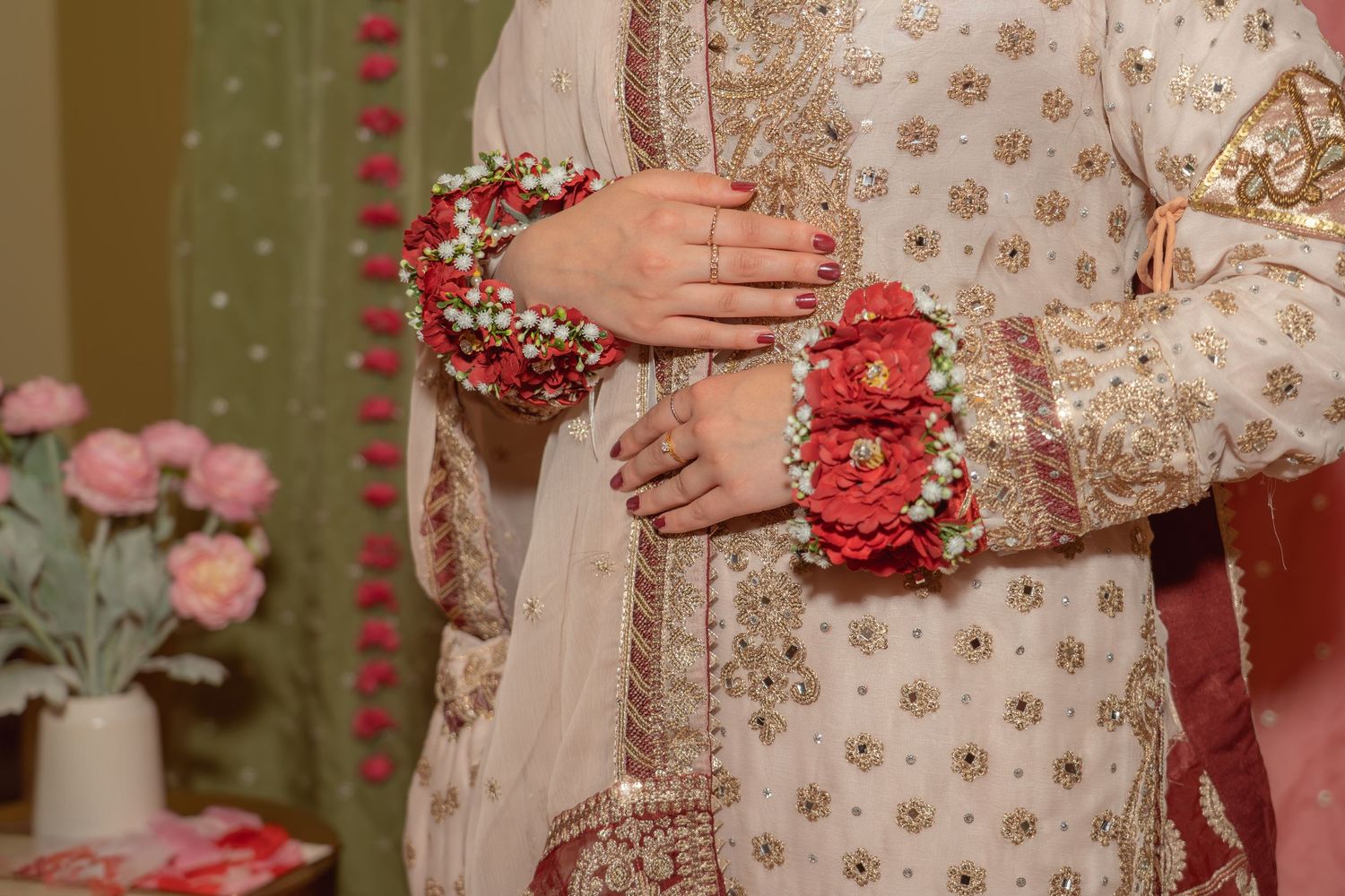 Close-up of bride and groom in traditional South Asian wedding attire with floral wrist decorations and embroidered garments.