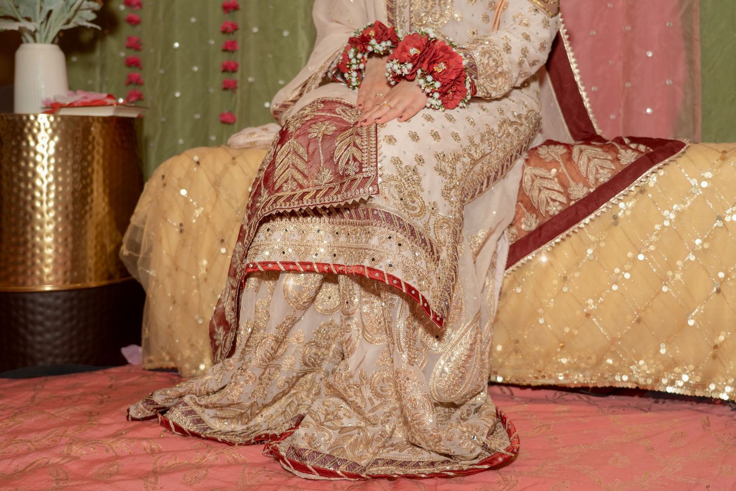 Bride in ornate cream and red embroidered bridal lehenga with floral hair accessories at a traditional South Asian wedding.