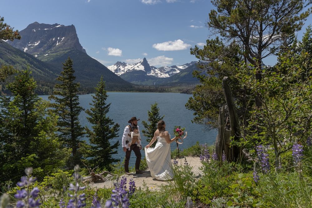 Bride and groom share a romantic moment overlooking a stunning alpine lake surrounded by lupines and mountains.