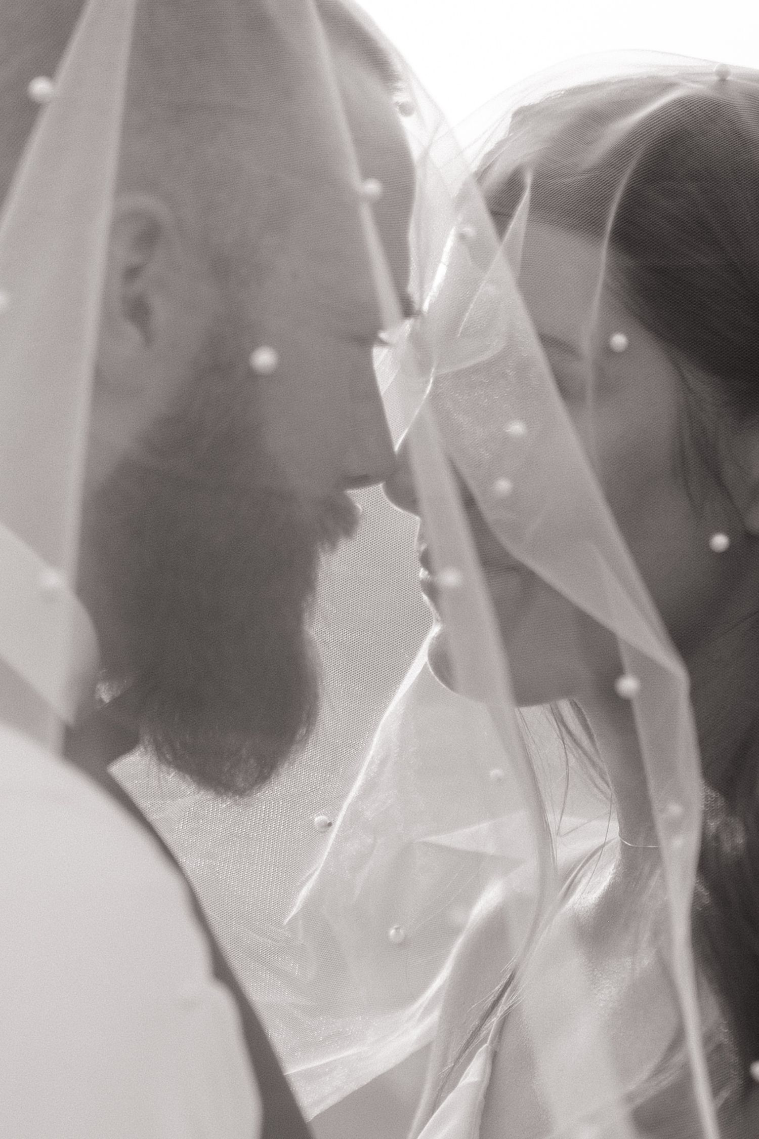 Black and white photo of a bearded groom kissing his bride under a pearl-adorned wedding veil in Northern California.