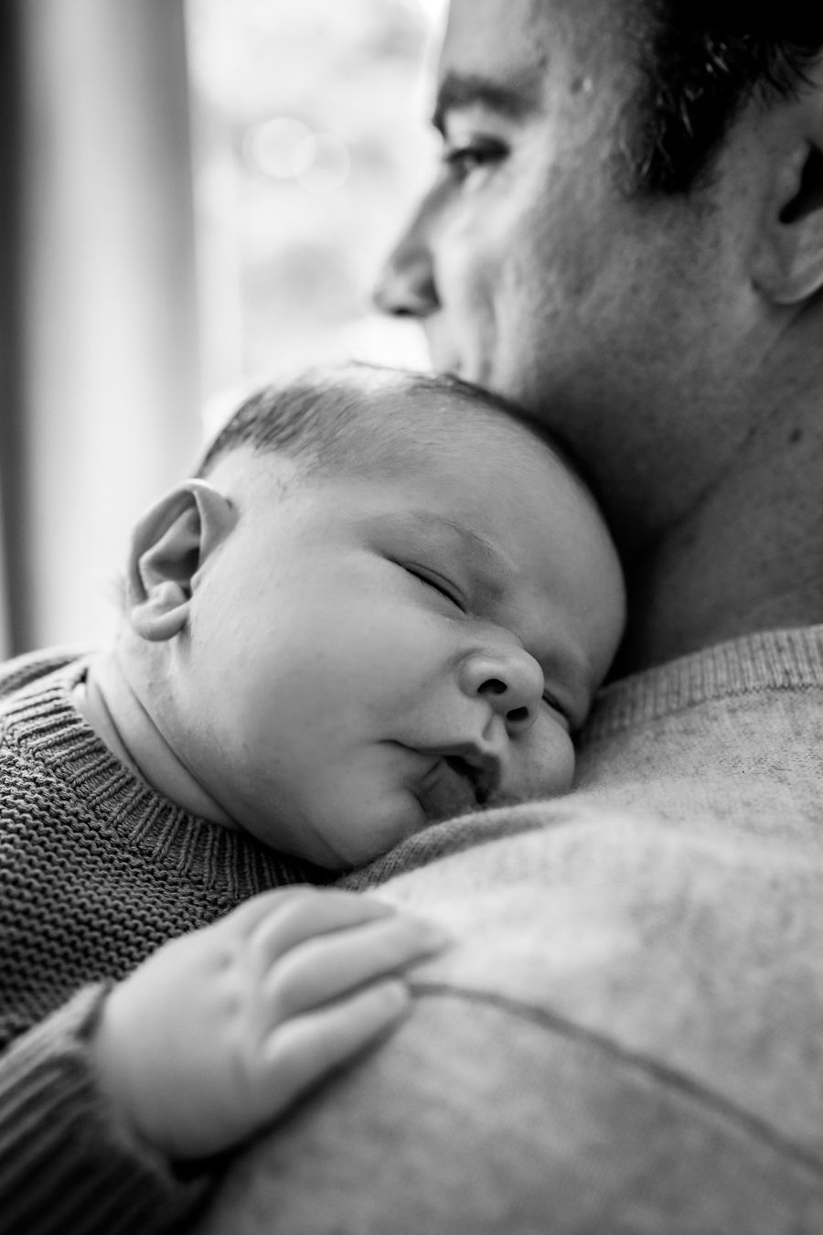 Black and white photo of a sleeping newborn baby resting peacefully on a parent's chest.