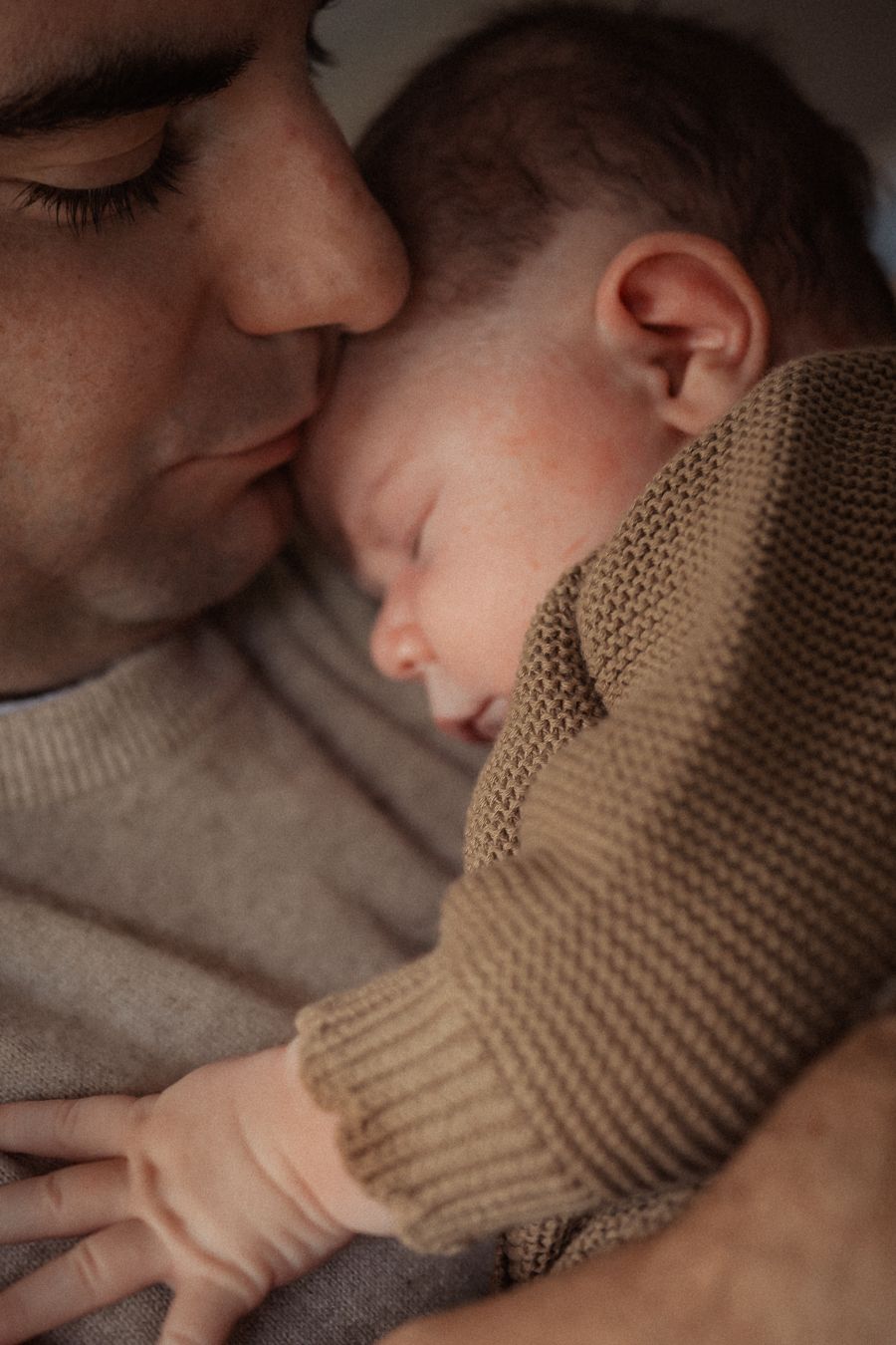 A father tenderly holds his sleeping newborn baby dressed in a cozy knit sweater.