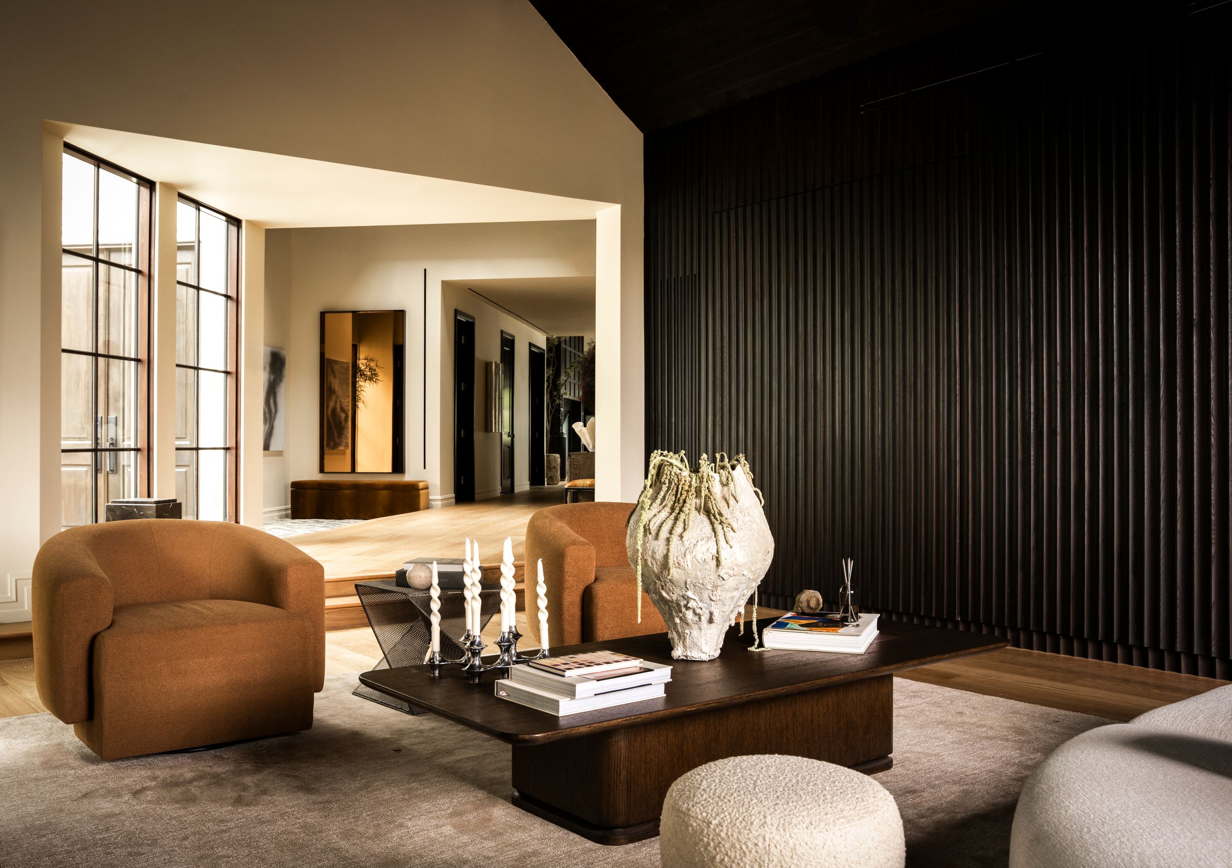 Modern living room with brown curved sofa, dark wood coffee table, textured vase, and elegant dark slat wall accent.