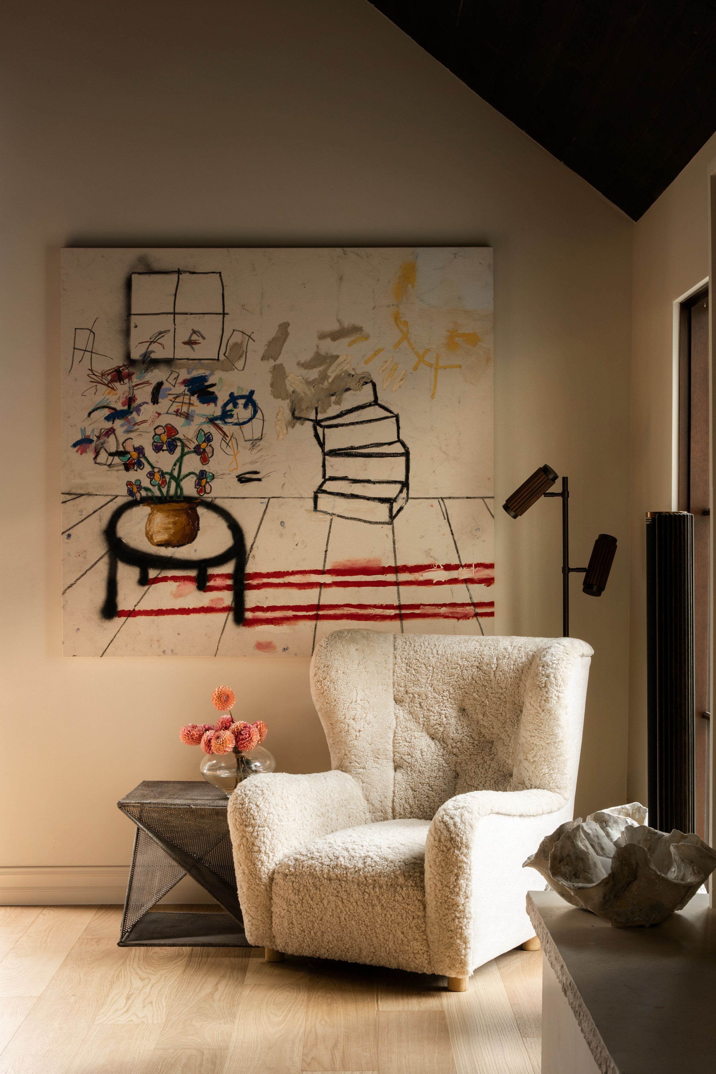 Cozy reading nook with a shearling armchair, abstract wall art, and a small side table with pink flowers.