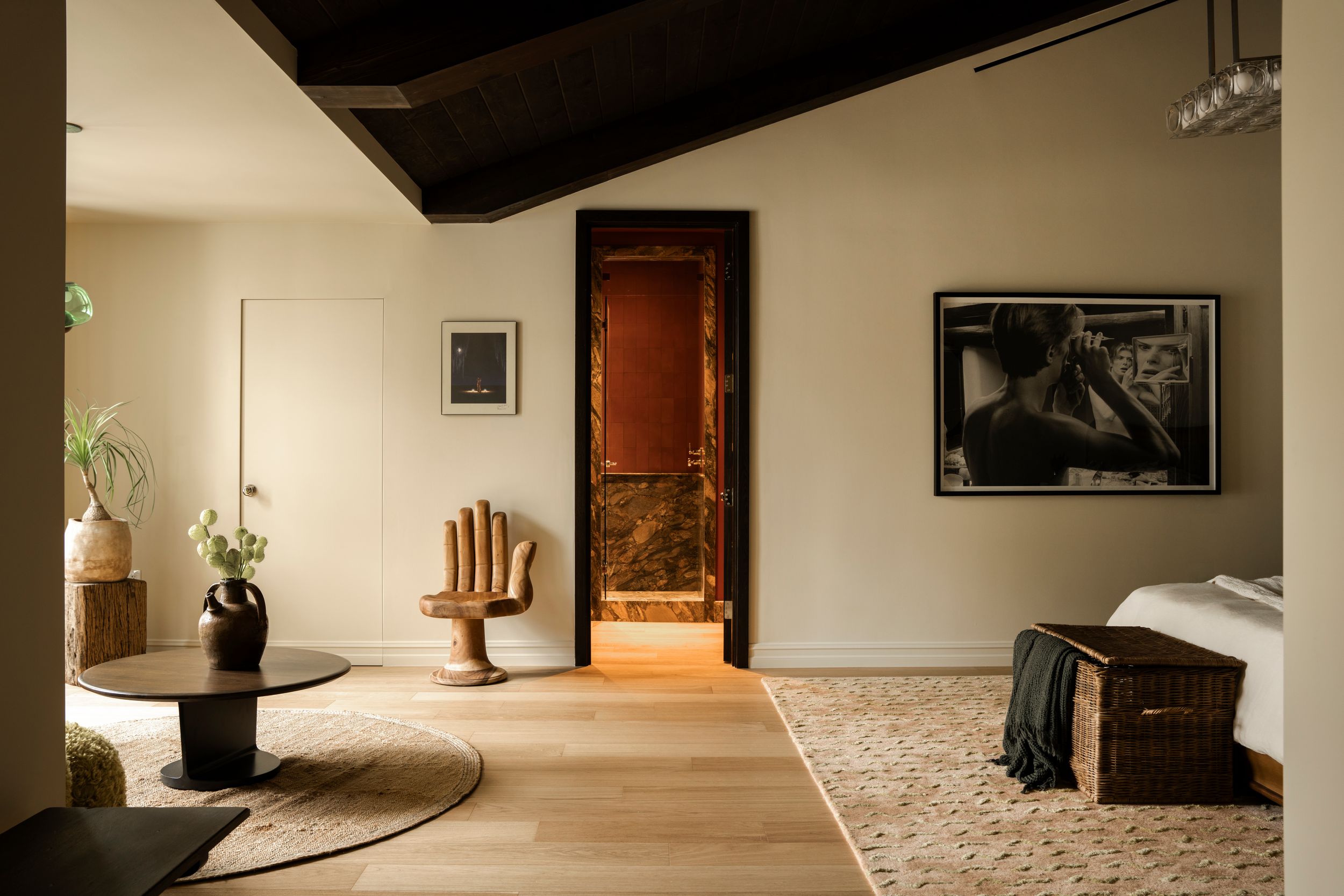 Modern bedroom with warm neutral tones, wooden furniture, abstract art, and an ornate doorway leading to a marble-accented room.