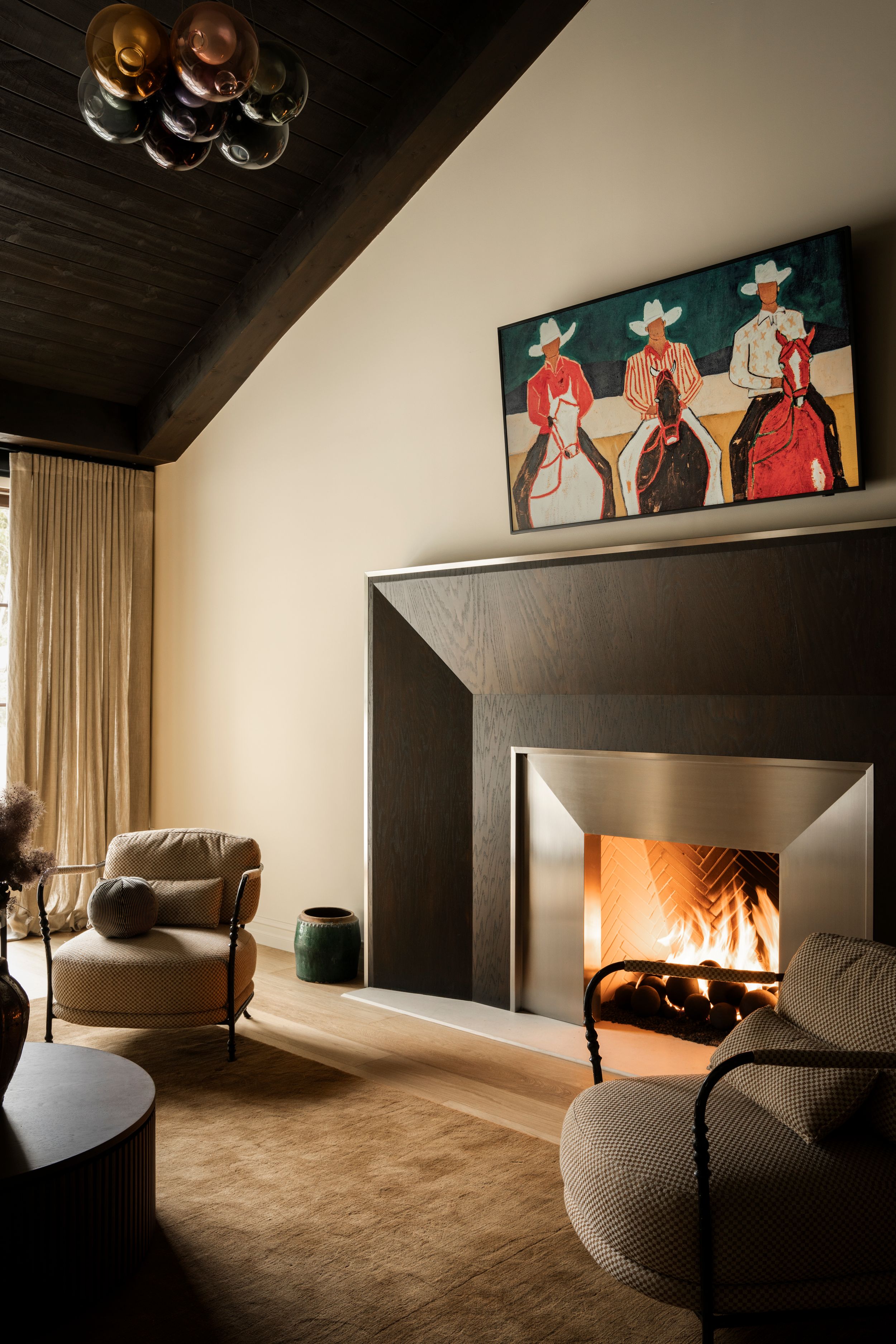 Elegant living room with a dark fireplace, cowboy-themed artwork, and neutral upholstered chairs.