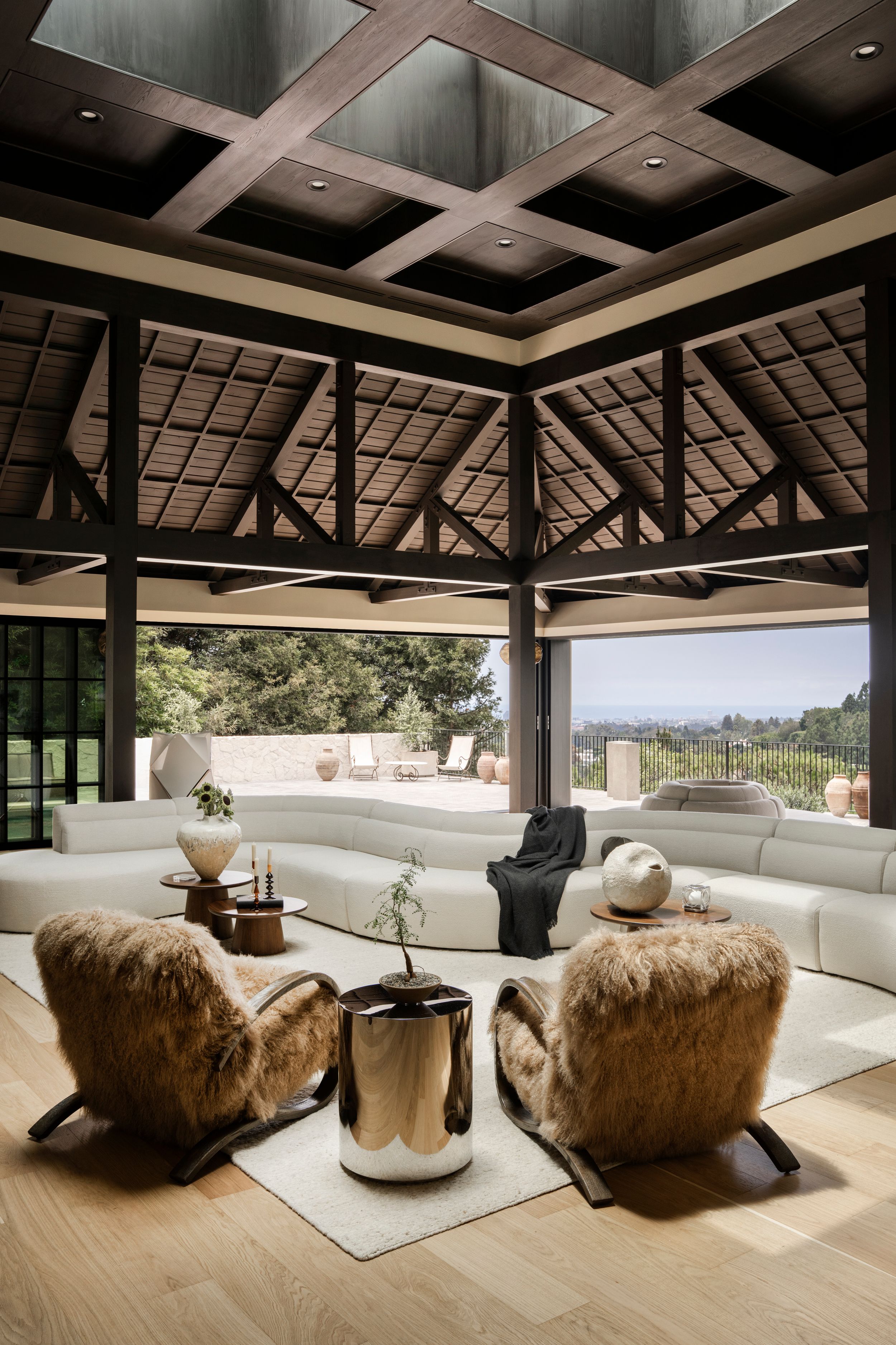 Spacious open-air lounge with fur chairs, white curved sofa, coffered ceiling, and panoramic views.