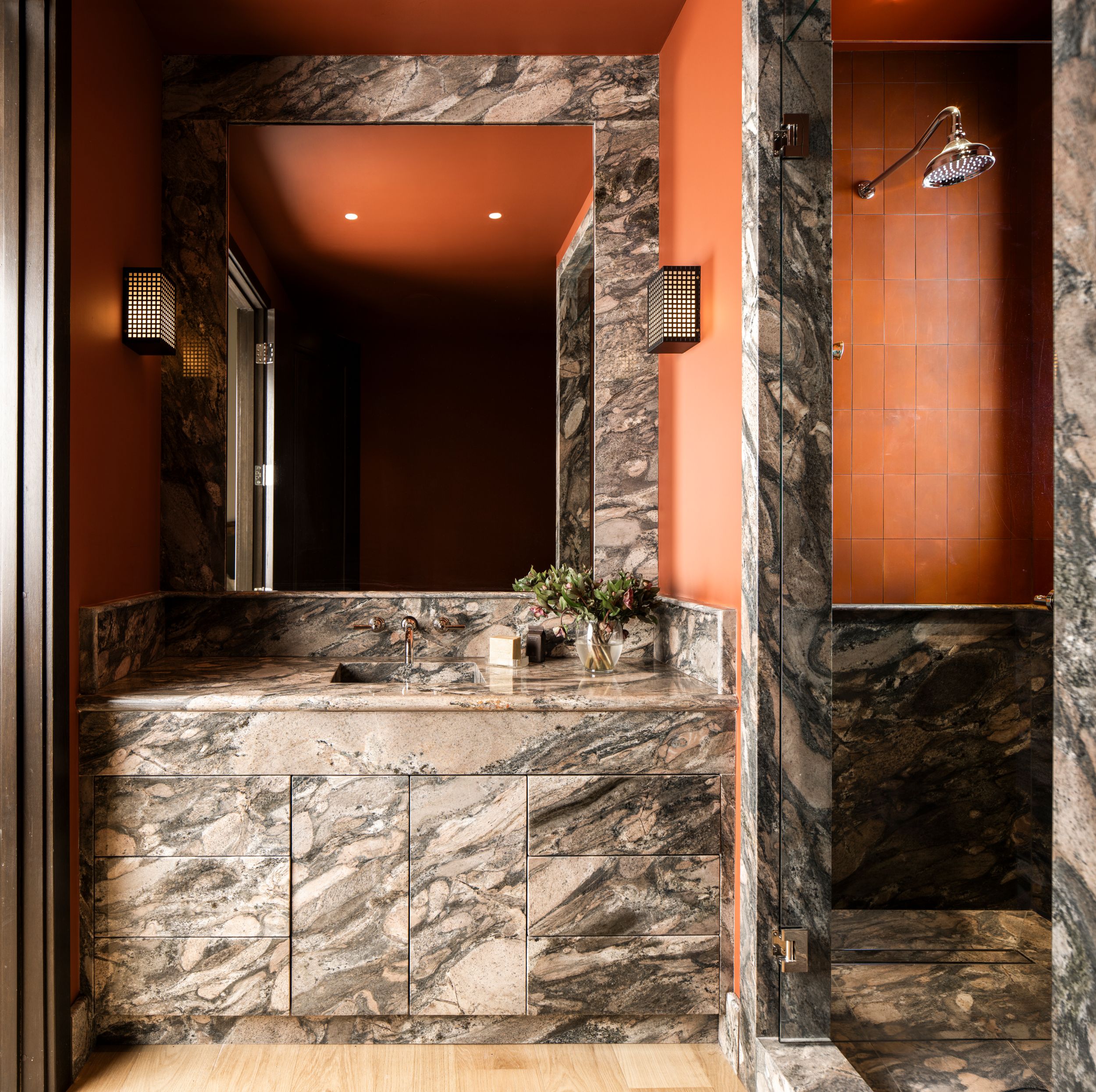 Luxurious bathroom vanity with dramatic marble surround, warm terracotta walls, and elegant wall sconces.