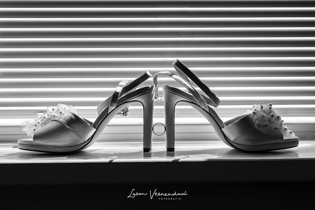 Zwart-wit detailfoto van Madeliefs trouwschoenen met de ring ertussen