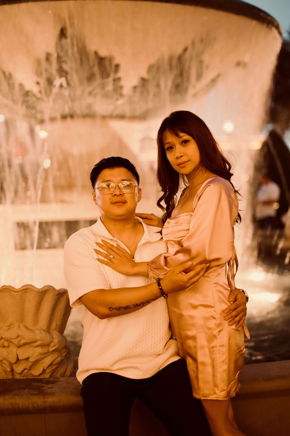 Couple posing affectionately in front of a illuminated fountain at night.