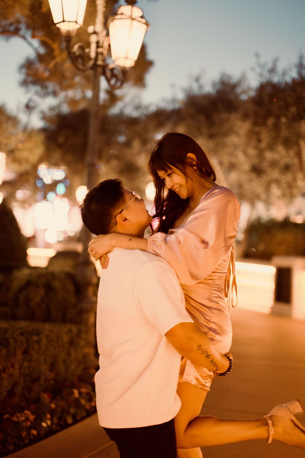 Man lifting woman in his arms as they share a joyful embrace under evening street lights outdoors.