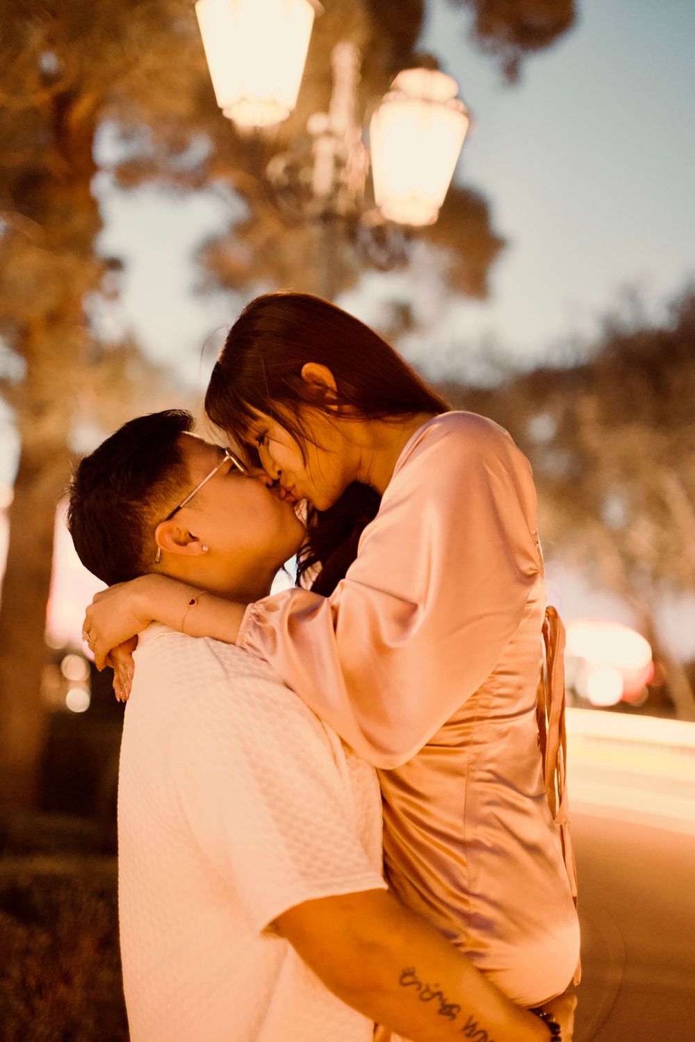 Couple sharing a tender kiss under a glowing street lamp during a romantic evening outdoors.