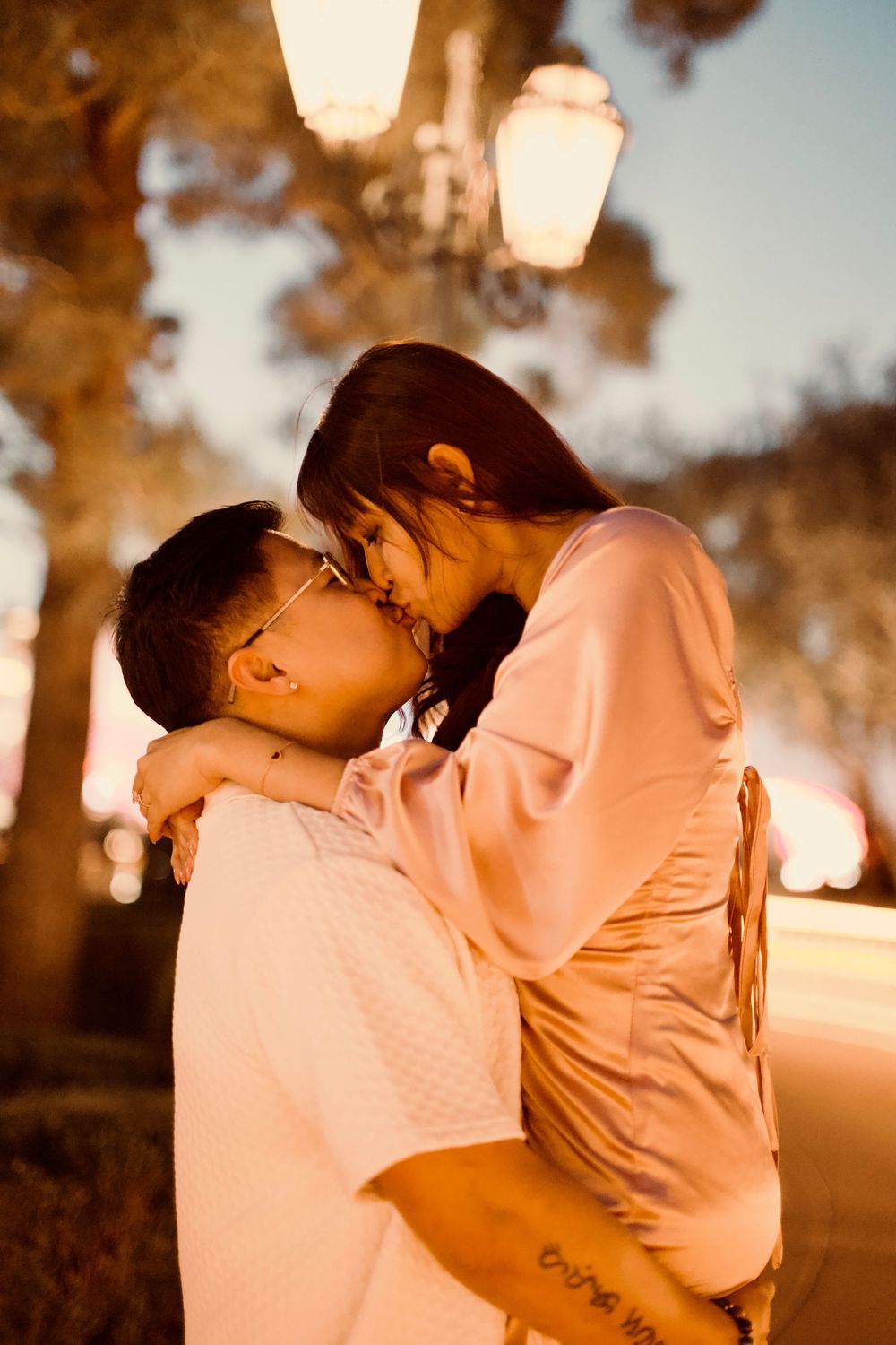 A couple shares a tender kiss under a glowing street lamp during a romantic evening outdoors.