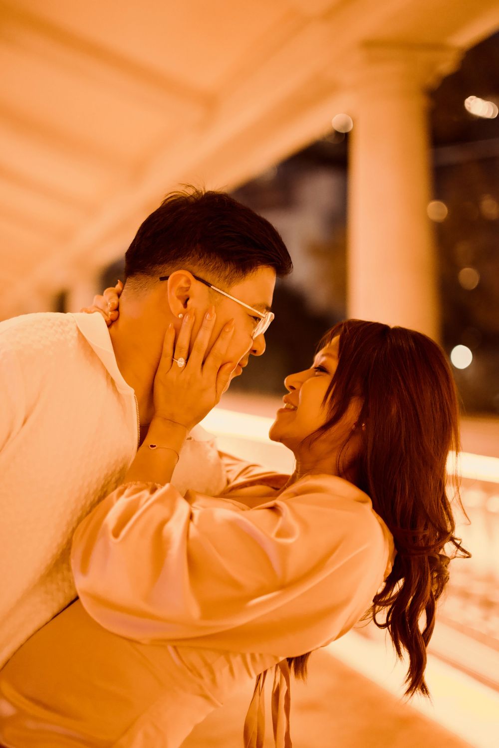 Couple sharing a tender romantic moment under warm golden lights at night.