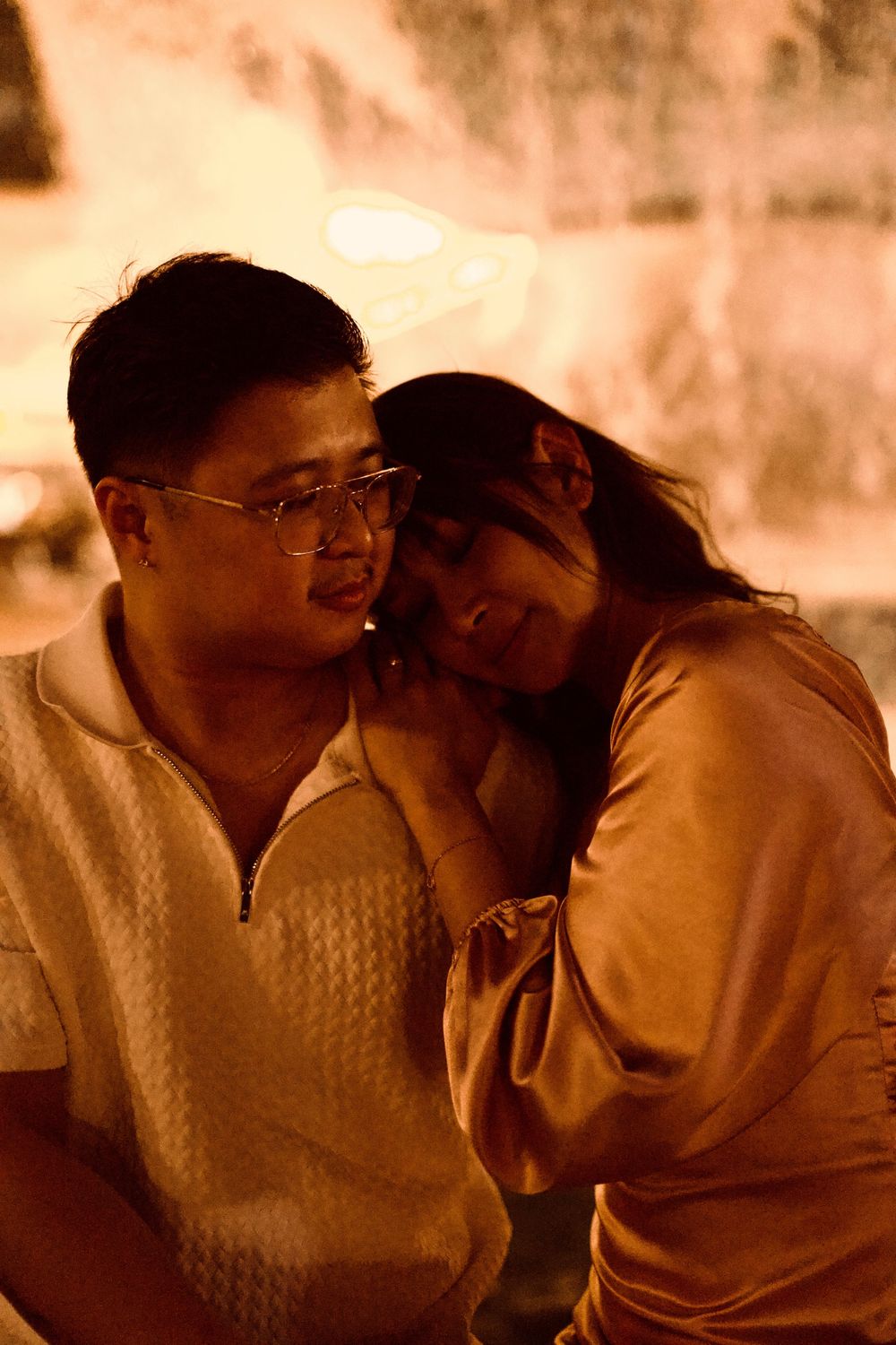 A couple shares an intimate moment, woman resting her head on man's shoulder in warm golden light.