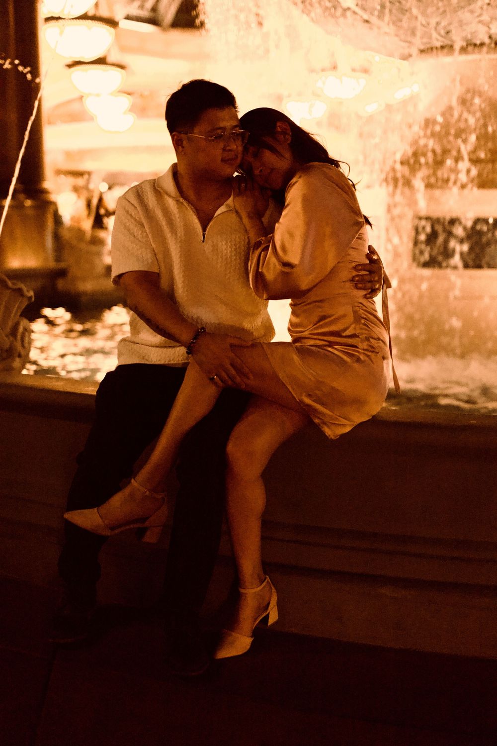Romantic couple sharing an intimate moment by a glowing fountain at night in Las Vegas.