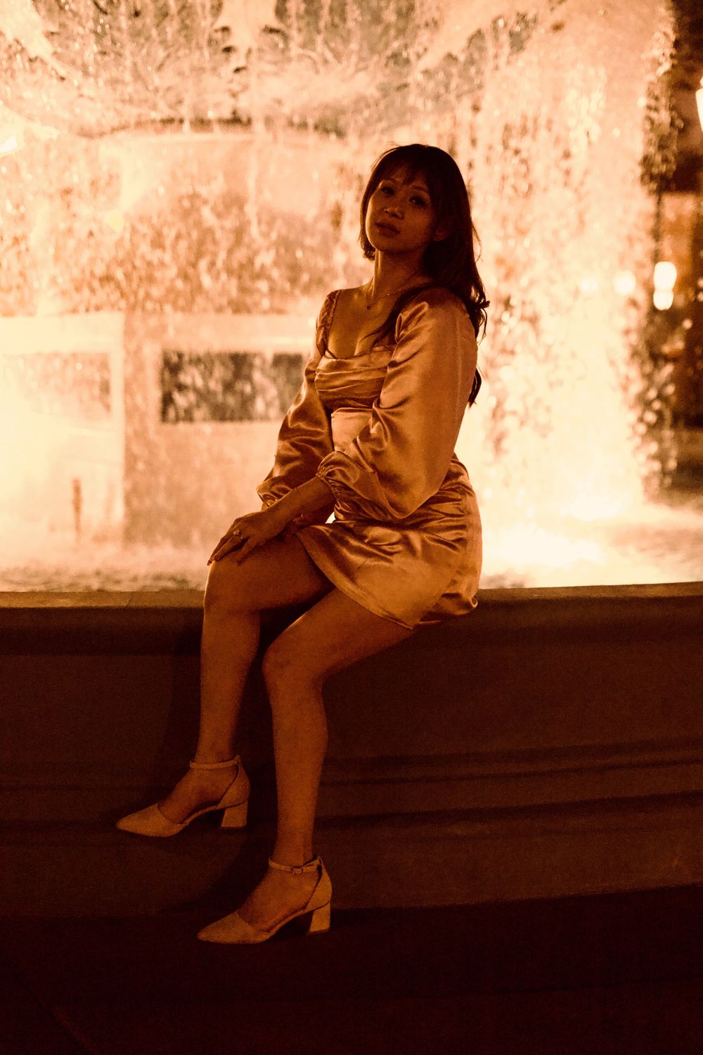 Woman in gold satin dress sitting on fountain edge at night.