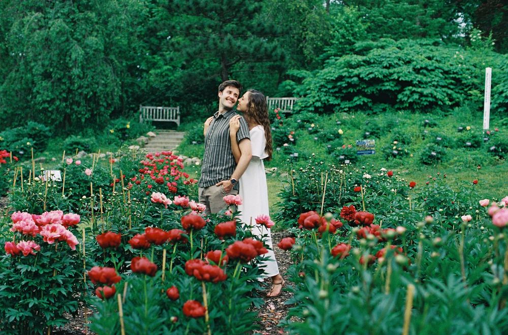 Romantic couple embracing in a vibrant garden filled with red and pink peony flowers.
