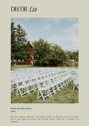 White wooden folding chairs arranged in rows on green grass for an outdoor wedding ceremony near a red barn.