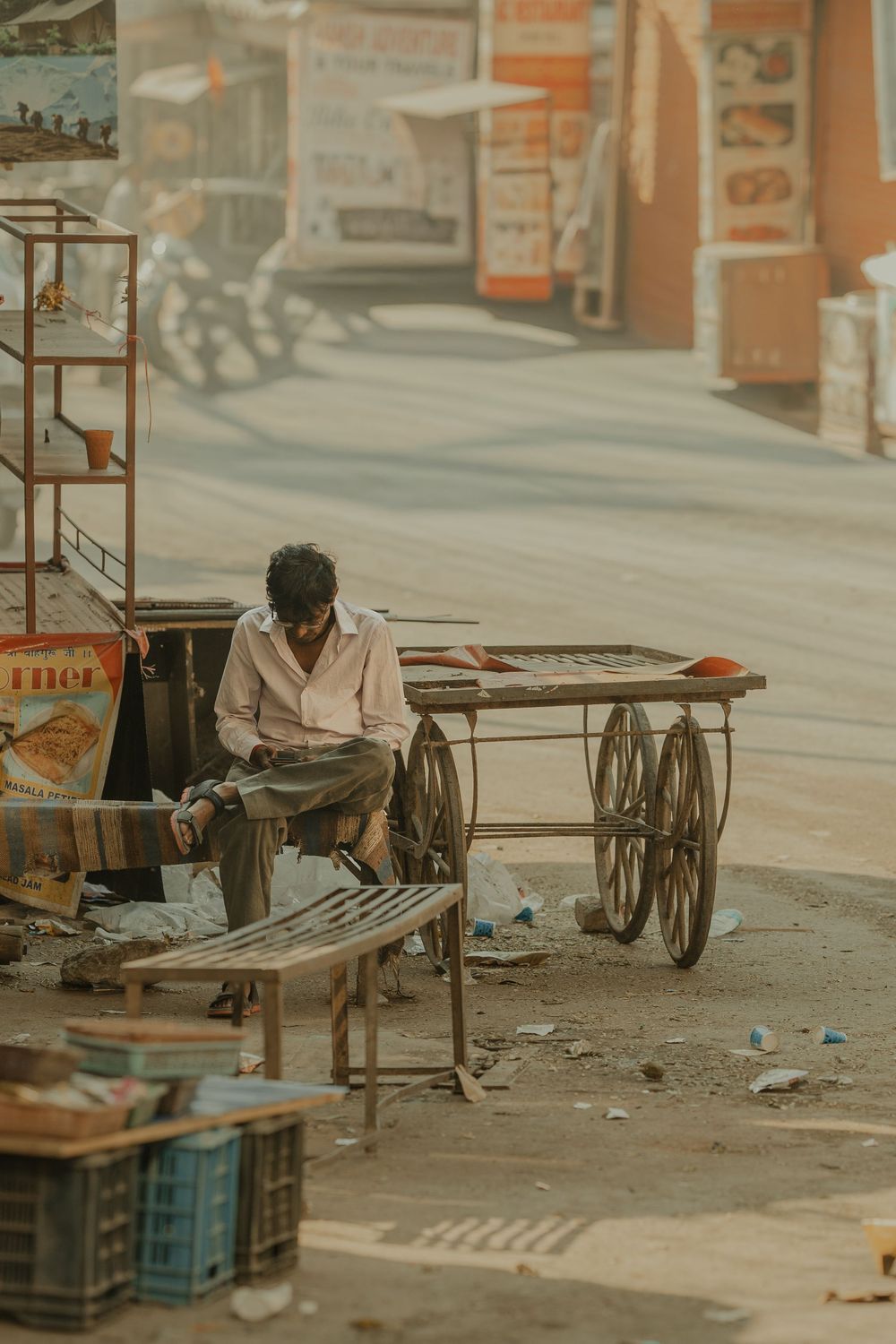 A weary man rests beside a wooden cart on a dusty Indian street market.