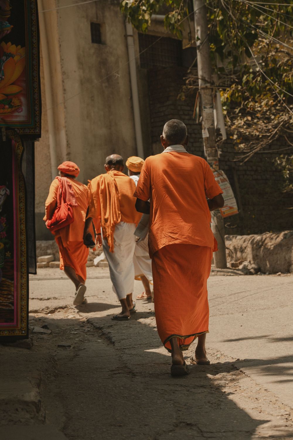 Hindu monks in orange robes walk down a narrow sunlit street in India.