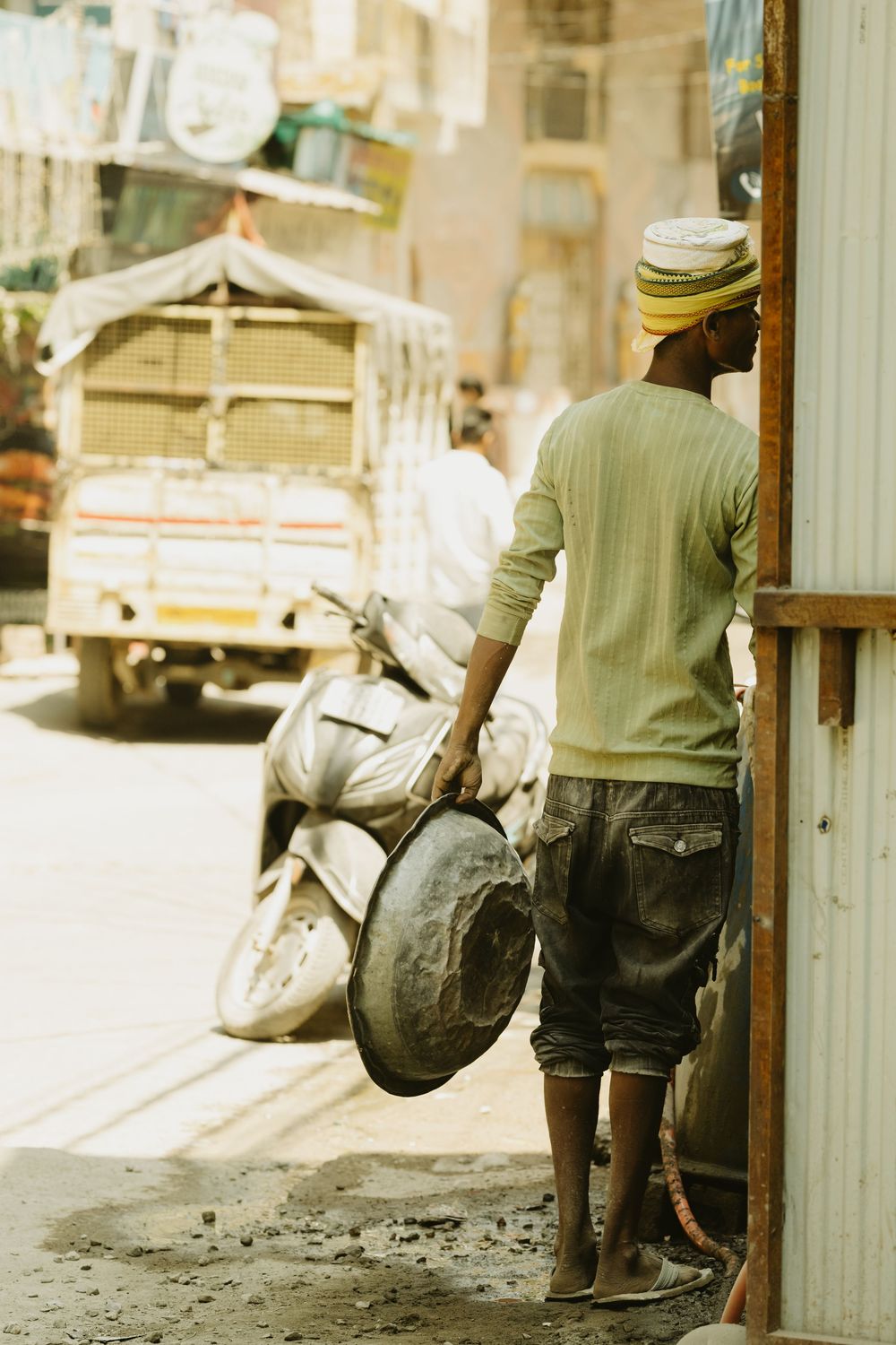 Young Indian man in turban holding a metal pan while leaning against a doorway.