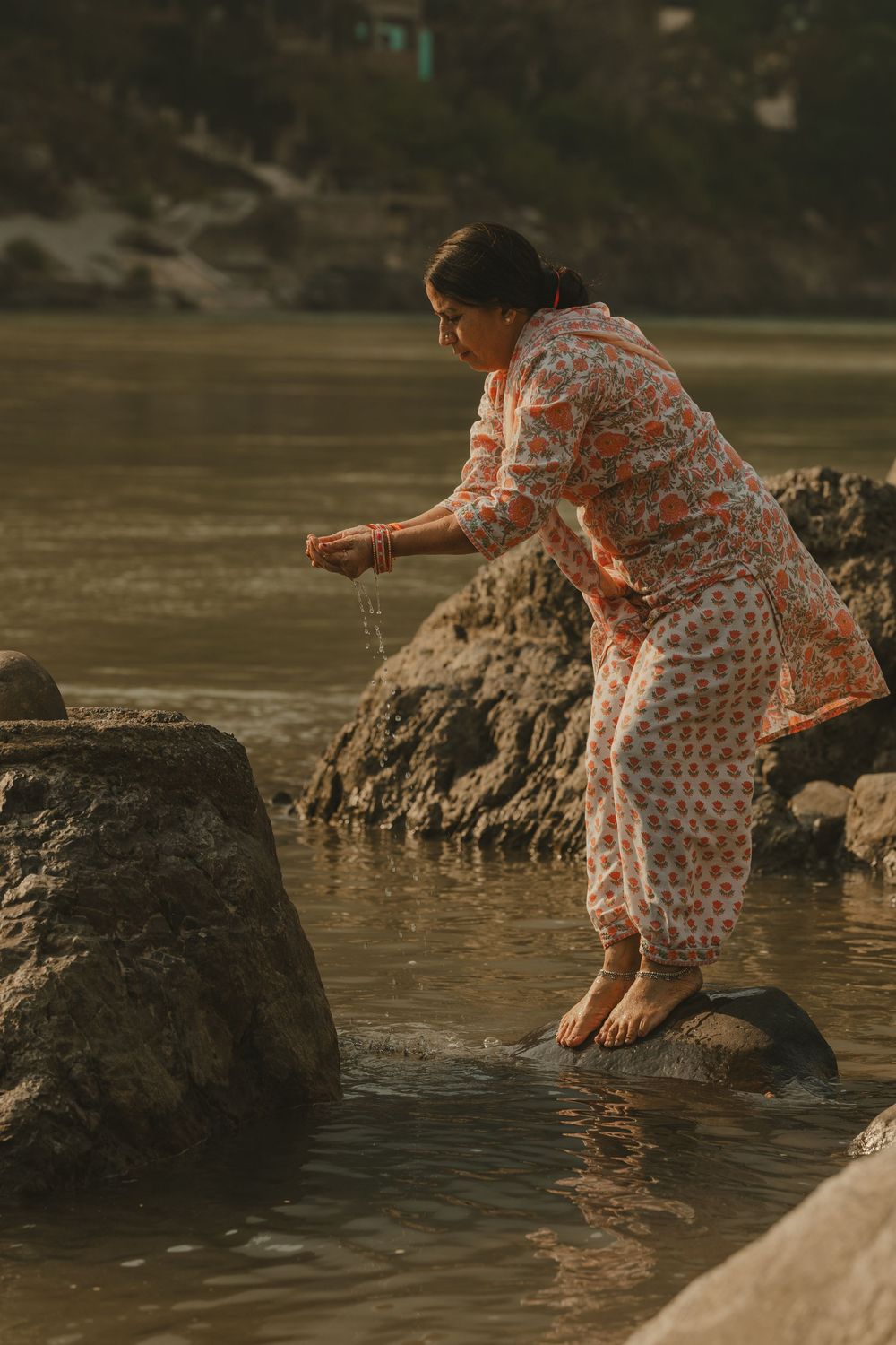 A woman in traditional Indian dress performs a ritual by a sacred river.