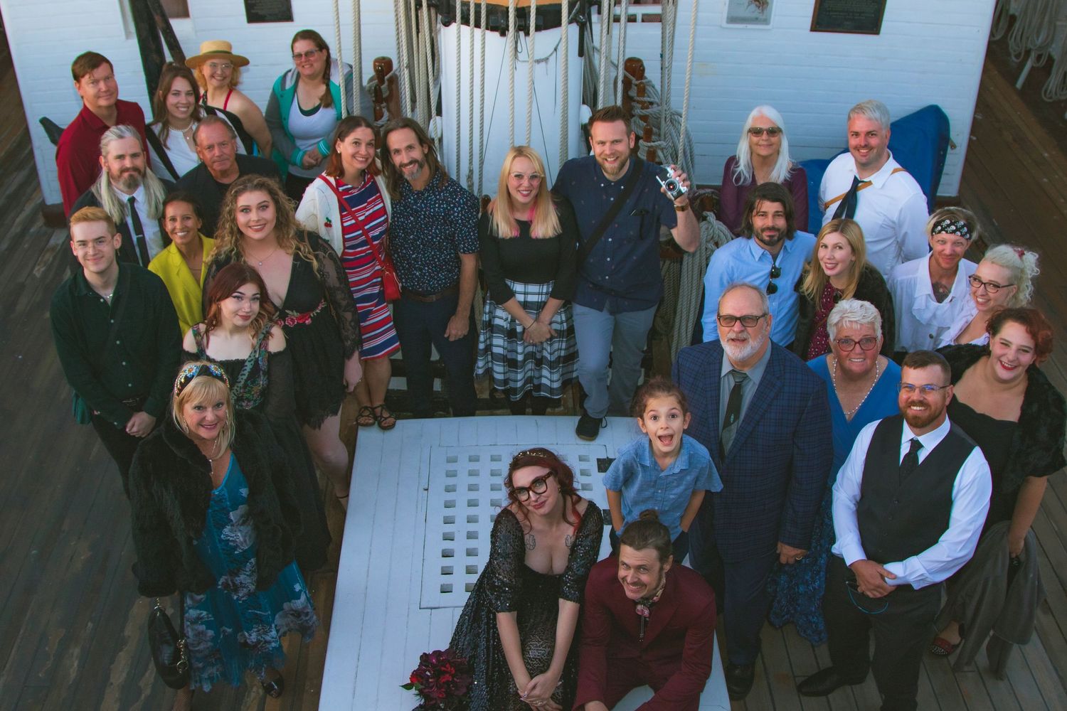 Large group of smiling adults and children posing together indoors for a formal group photo.