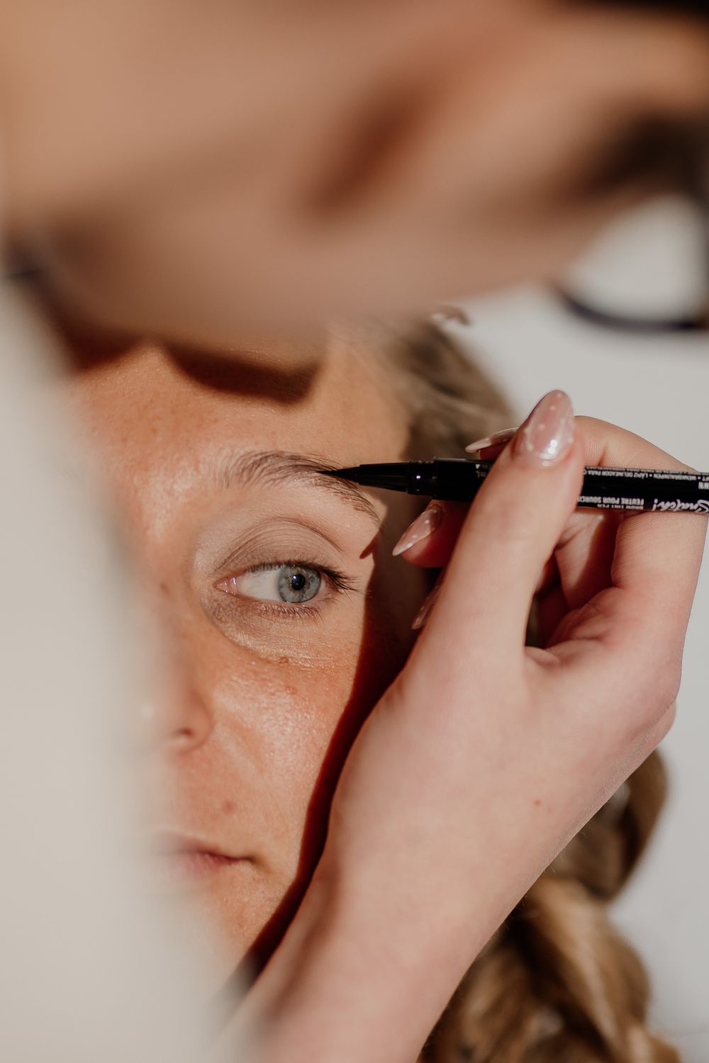 Makeup artist applying black eyeliner to a freckled woman with blue eyes during a beauty session.