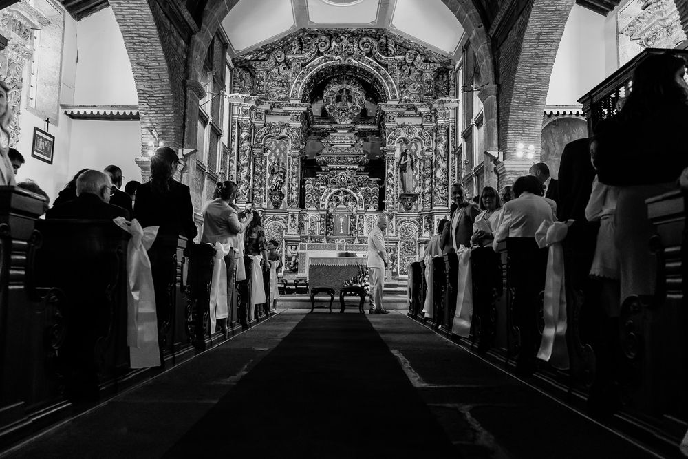 Black and white photo of a wedding ceremony inside an ornate church with guests seated in pews.