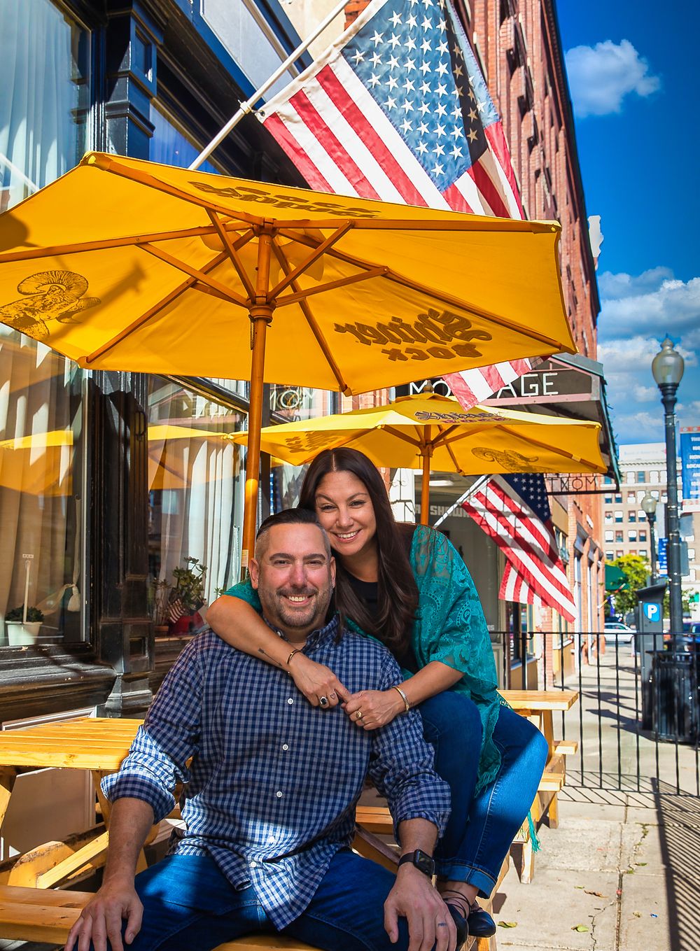 Outdoor cafe scene with yellow umbrella and American flags on building facade.