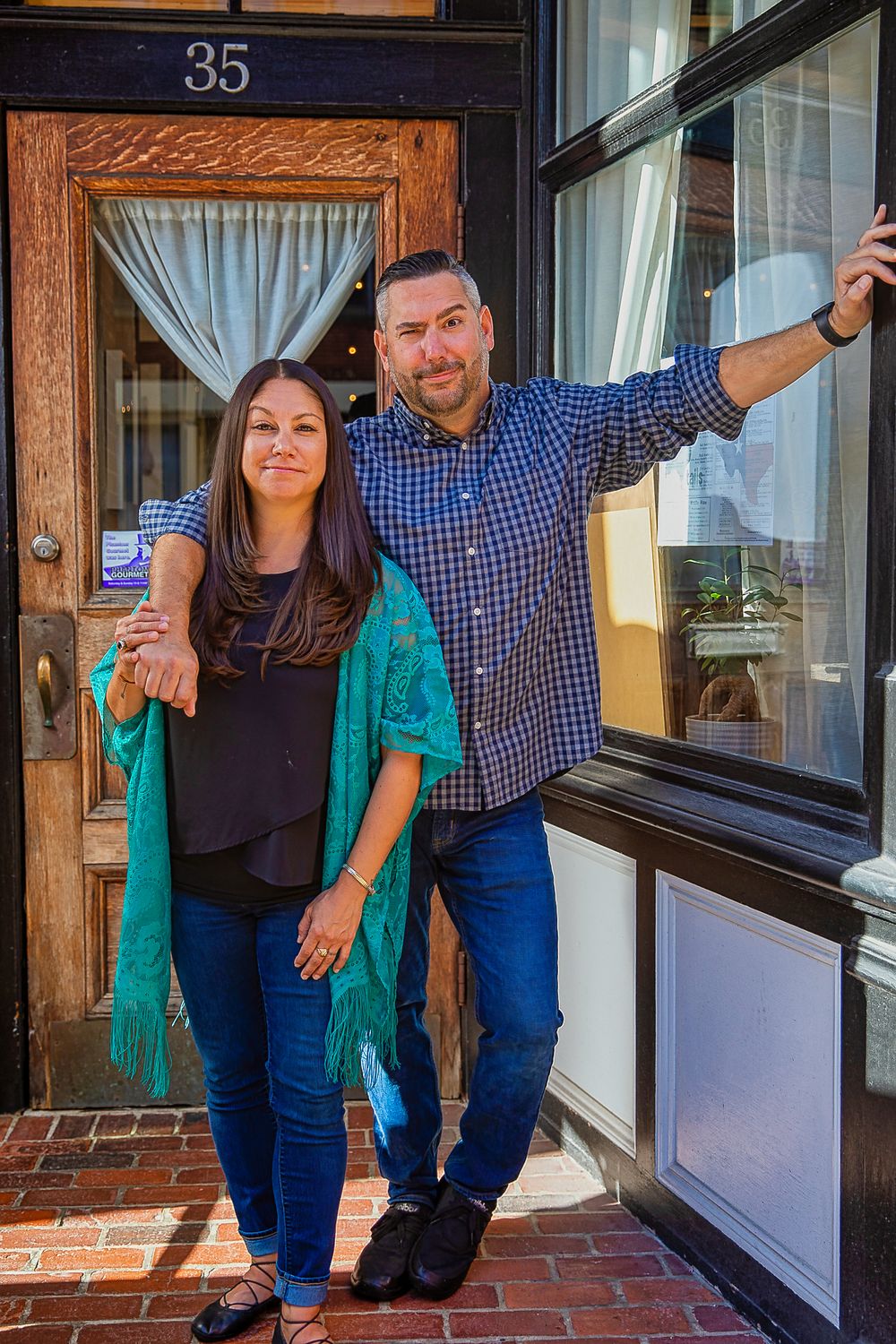 Couple in blue and green outfits posing playfully in front of a storefront window.