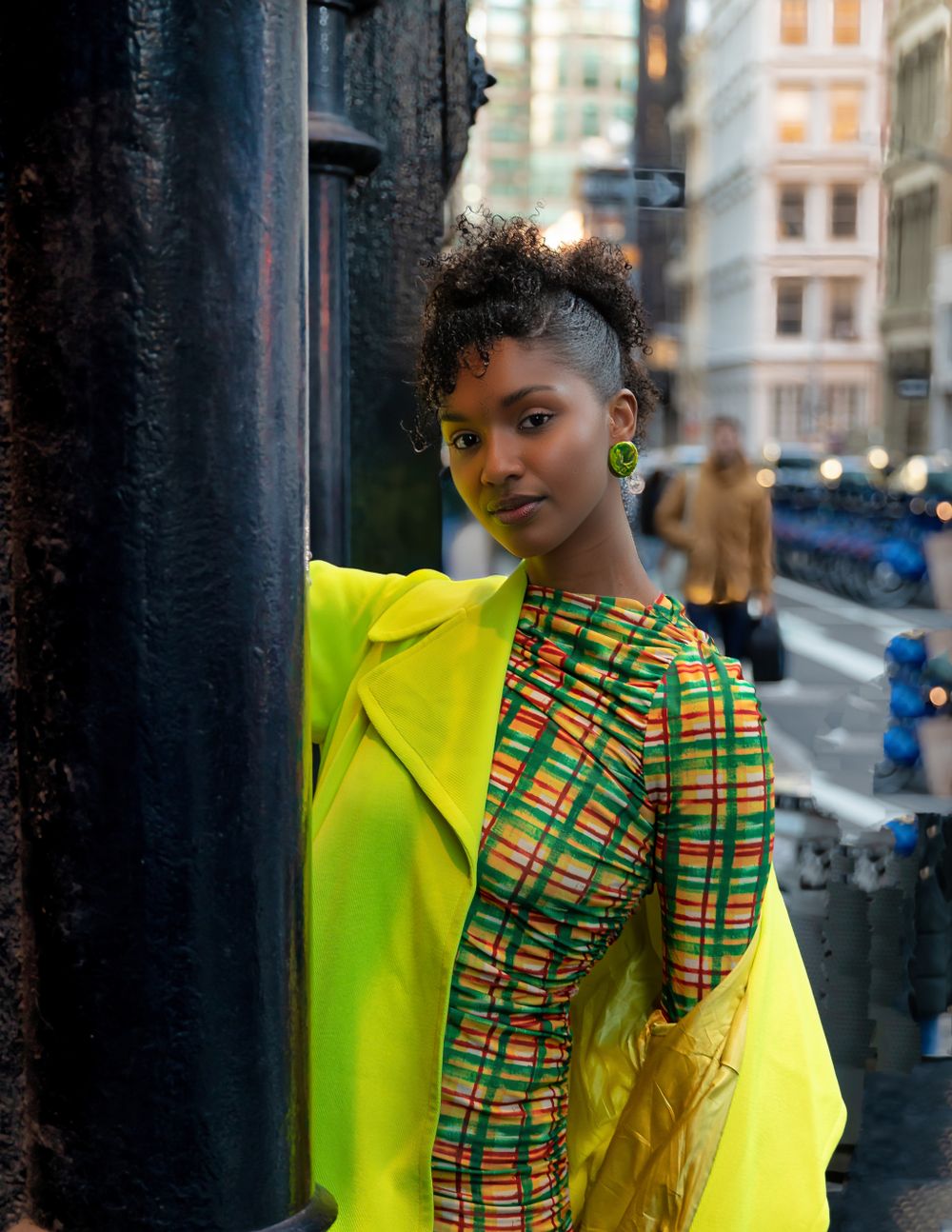 Street style shot featuring bright yellow jacket and African print fabric against urban backdrop.