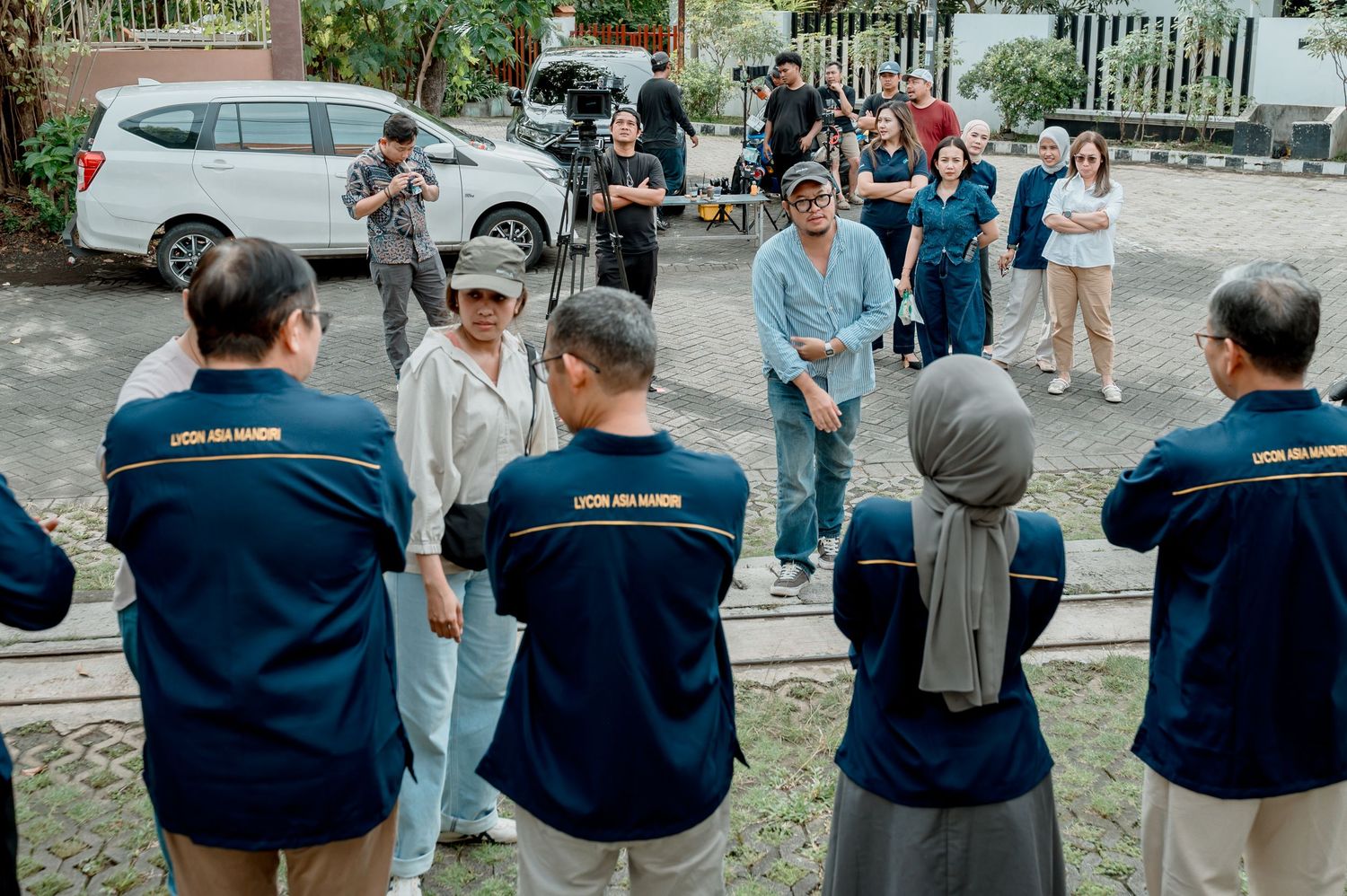 A group of people in matching navy blue jackets gather outdoors in a circle during a team meeting or briefing.