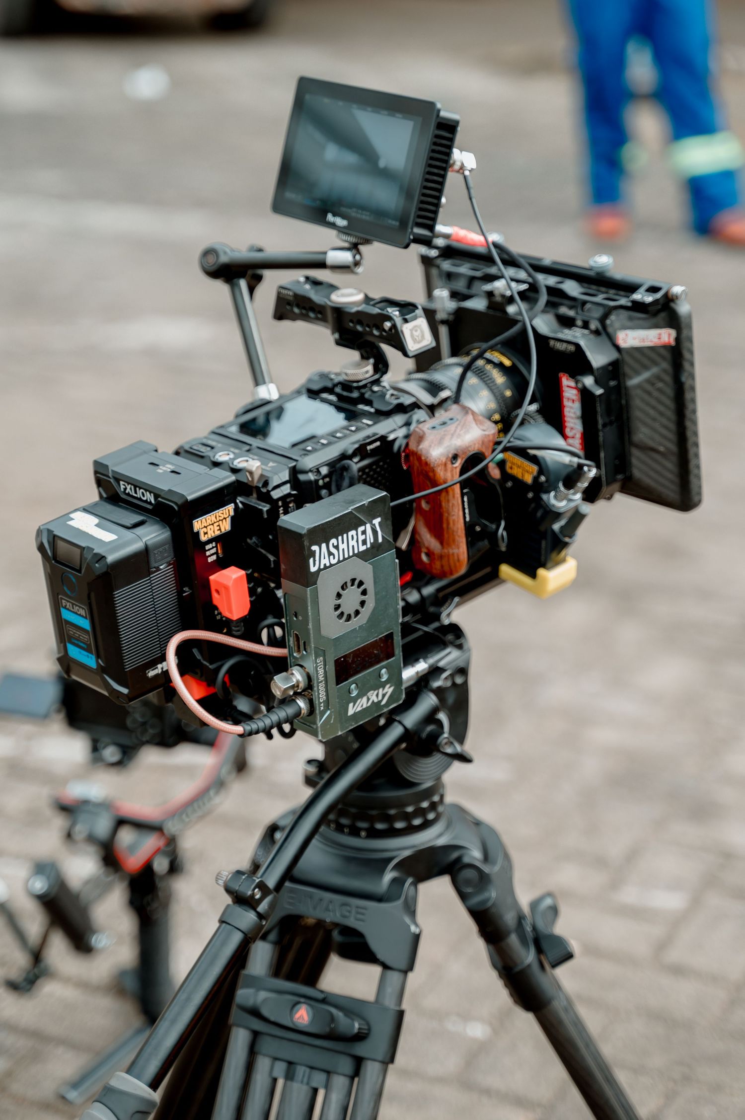Professional cinema camera on tripod with monitor, matte box, and battery pack on an outdoor film set.