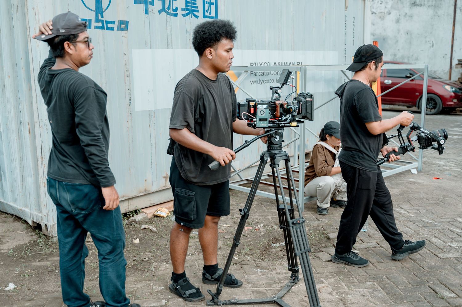Three filmmakers in black clothing operating a professional camera on a tripod at an outdoor film production set.