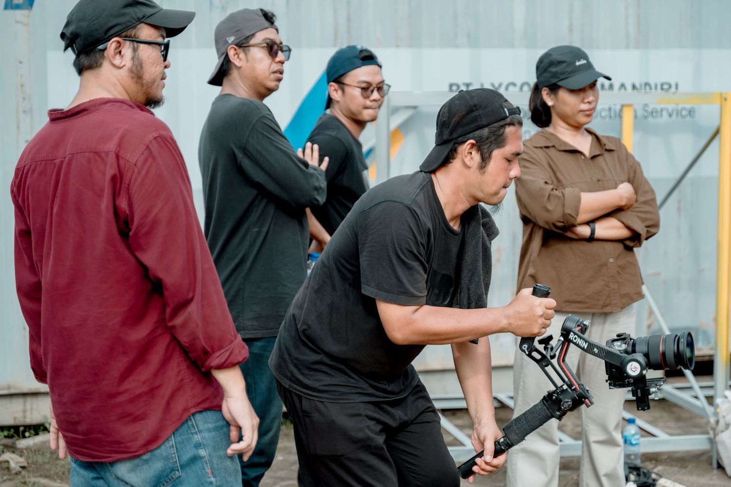 Film crew collaborating outdoors with a cameraman operating a gimbal stabilizer on set.