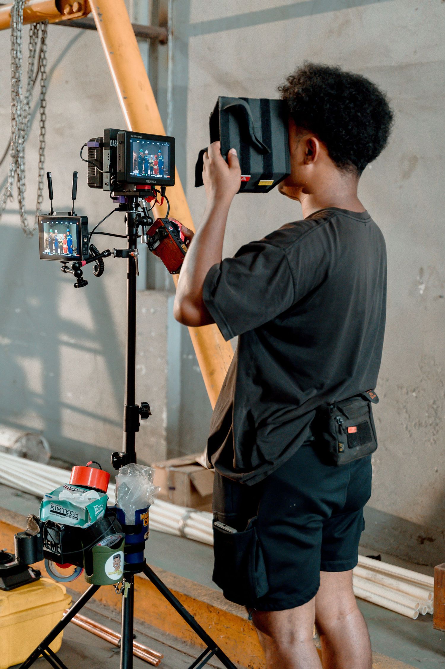 Young filmmaker operating a professional video camera on a tripod in an industrial studio setting.