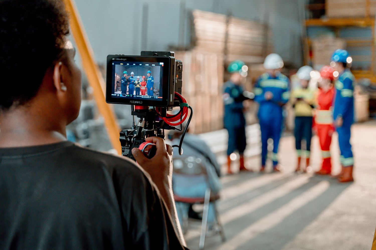Cameraman filming a group of workers in colorful safety gear inside an industrial warehouse during a video production shoot.