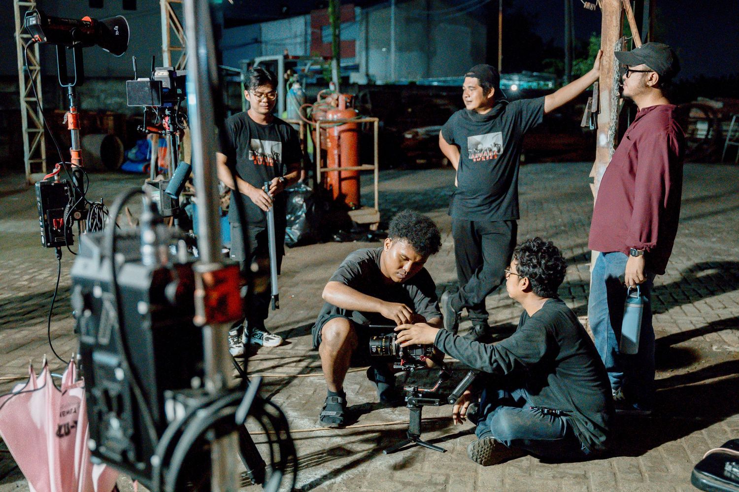 Film crew working together on a night shoot, adjusting professional camera equipment on an outdoor set.