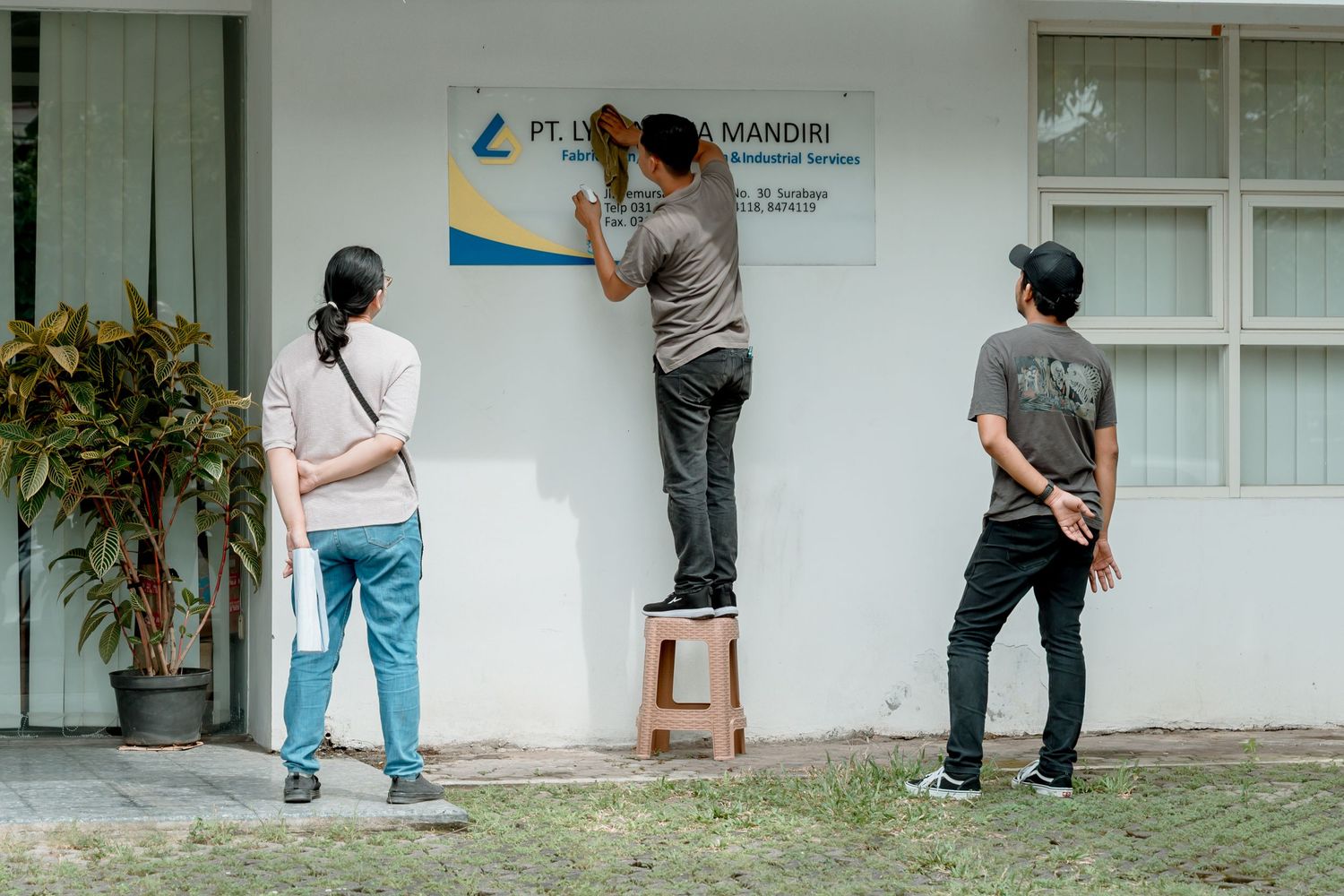 Workers installing a PT Len Industri Mandiri company sign on a white building exterior in Indonesia.