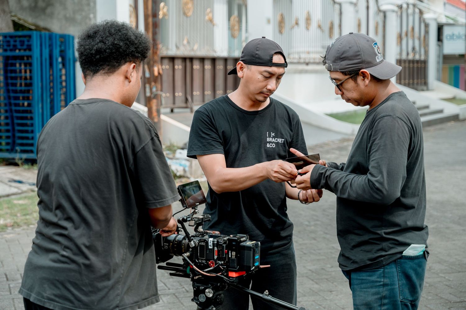 Three film crew members in black shirts reviewing camera equipment on a city street during a video production shoot.